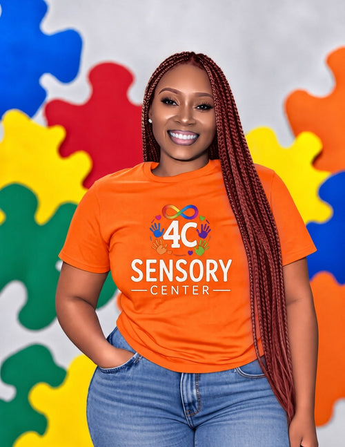 Woman wearing the orange 4C Sensory Center tee with jeans, in front of a colorful puzzle-piece backdrop